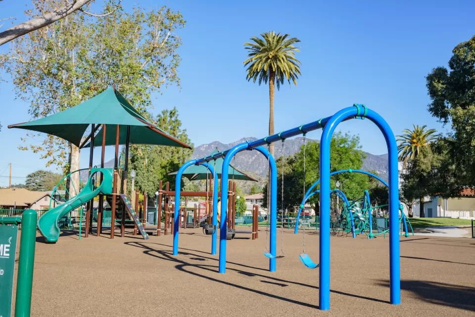 Blue and green playground equipment in Los Angeles with palm tree and mountains in background